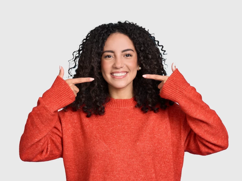 happy woman smiling pointing to her perfect teeth | general and cosmetic dentist in Oakland
